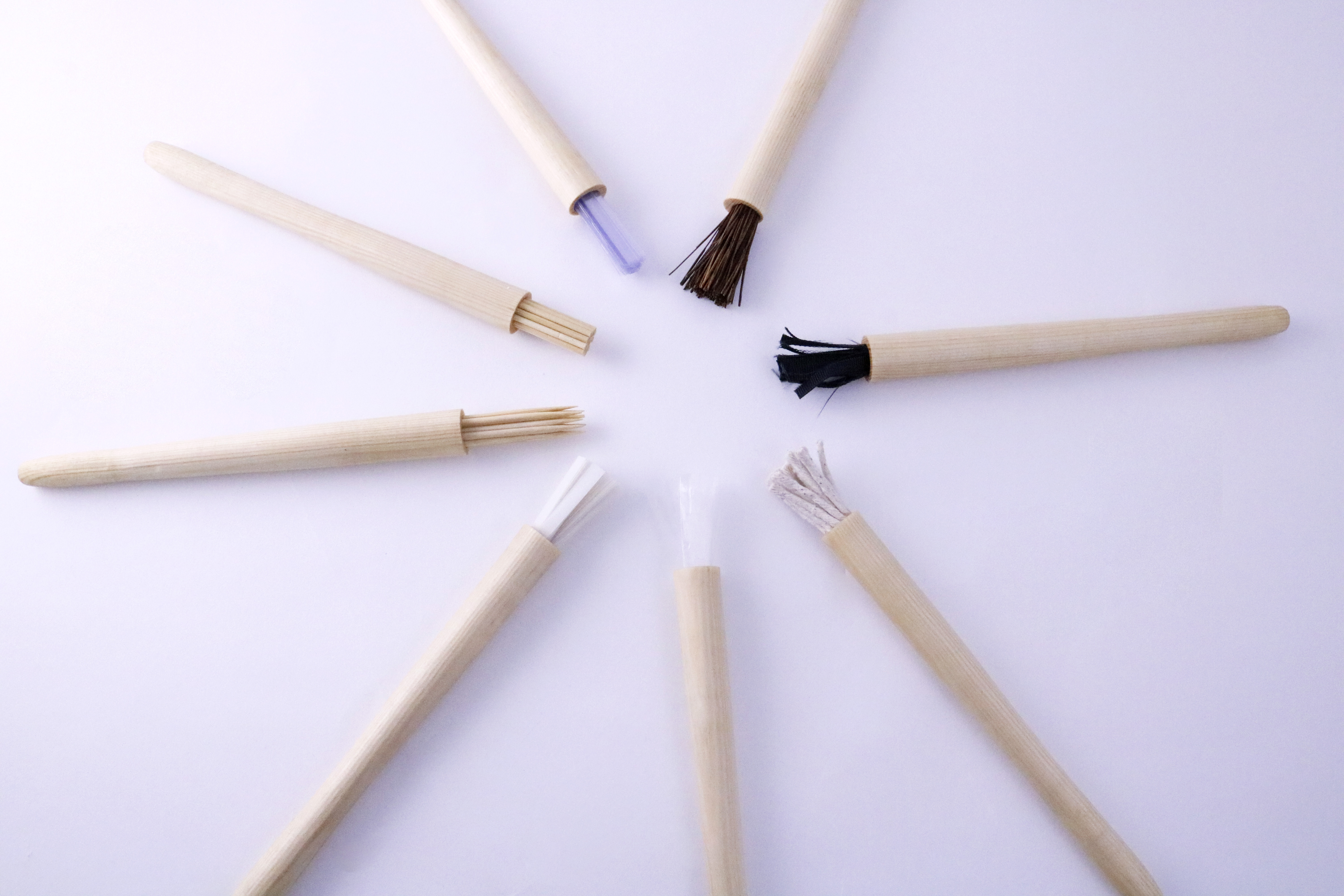 Eight brushes made of wood as the base, and different materials for the bristles on a purple background